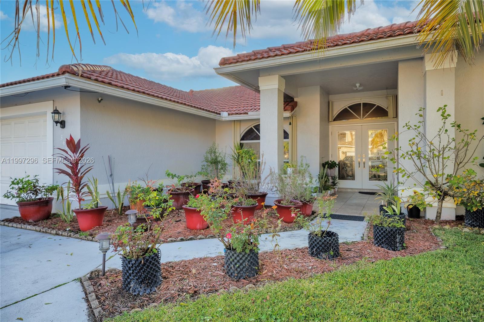 The exterior of a house features a tiled roof, a covered entryway, and numerous potted plants — 3462 Harness Cir # 0, Wellington FL 33449, WELLINGTON, FL