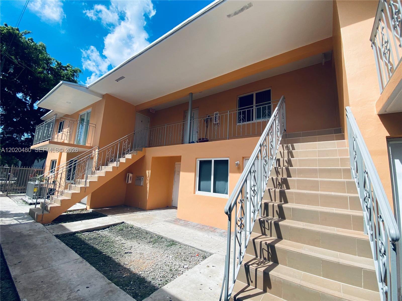 The exterior of a two-story orange apartment building features metal staircases and railings — 1121 NW 4  ST, Miami FL 33128, MIAMI, FL