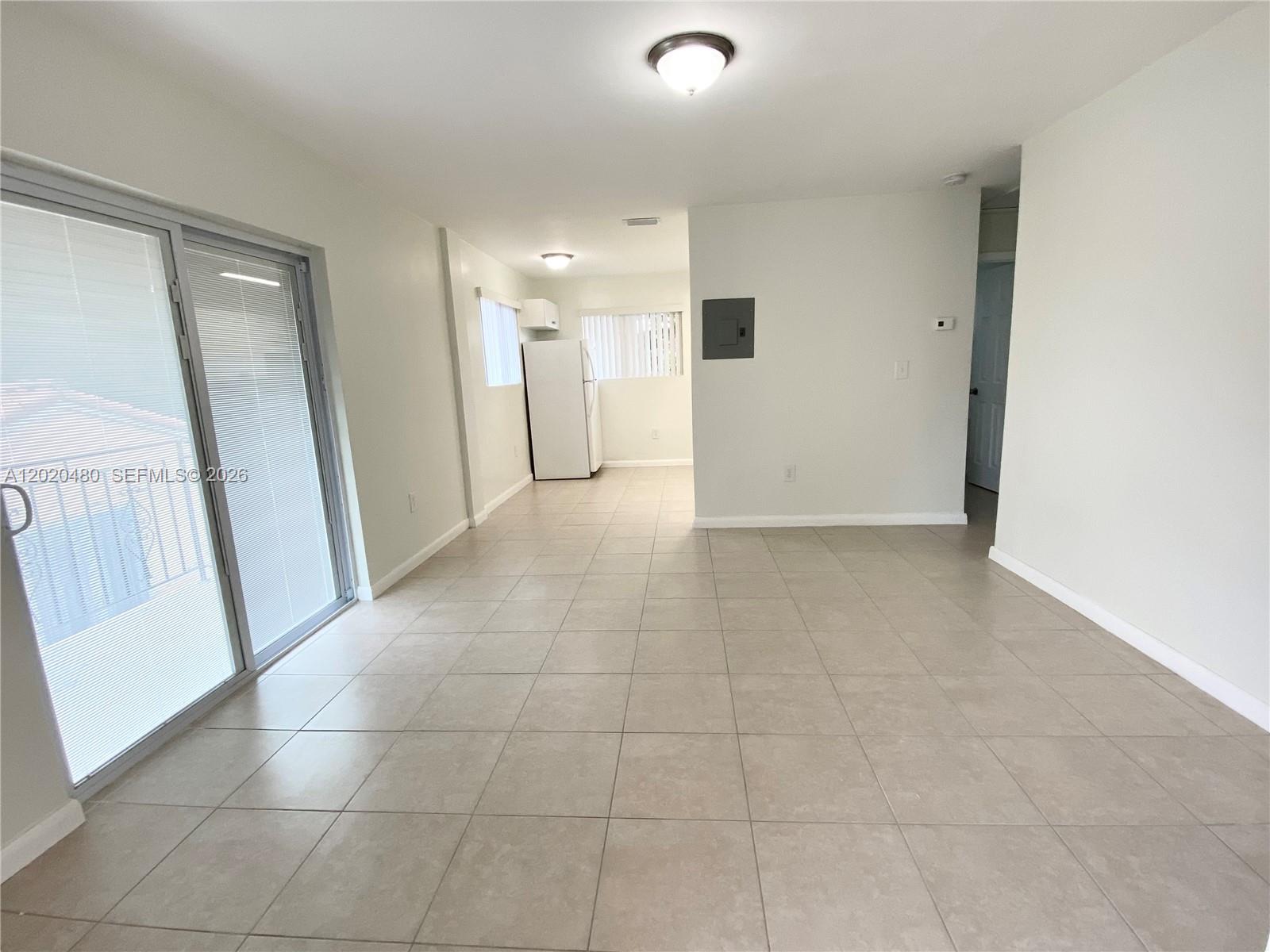 An open-concept living area features light-colored tile flooring, white walls, and a sliding glass door — 1121 NW 4  ST, Miami FL 33128, MIAMI, FL