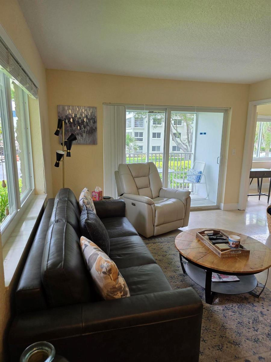 A living room features a dark leather sofa, a beige recliner, and a round coffee table — 207 Tropic Isle Drive # 215, Delray Beach FL 33483, DELRAY BEACH, FL