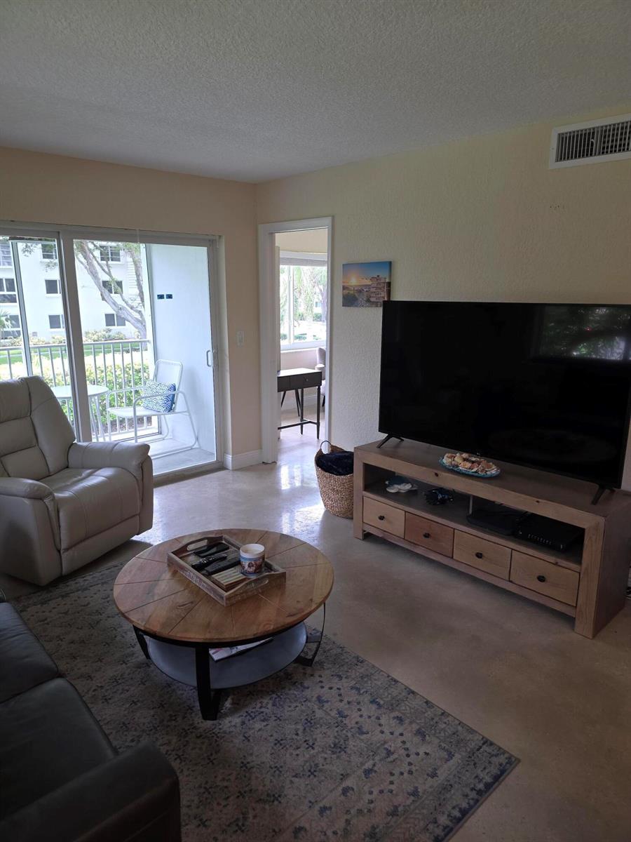 A living room features a television on a wooden stand, a round coffee table, and a recliner — 207 Tropic Isle Drive # 215, Delray Beach FL 33483, DELRAY BEACH, FL