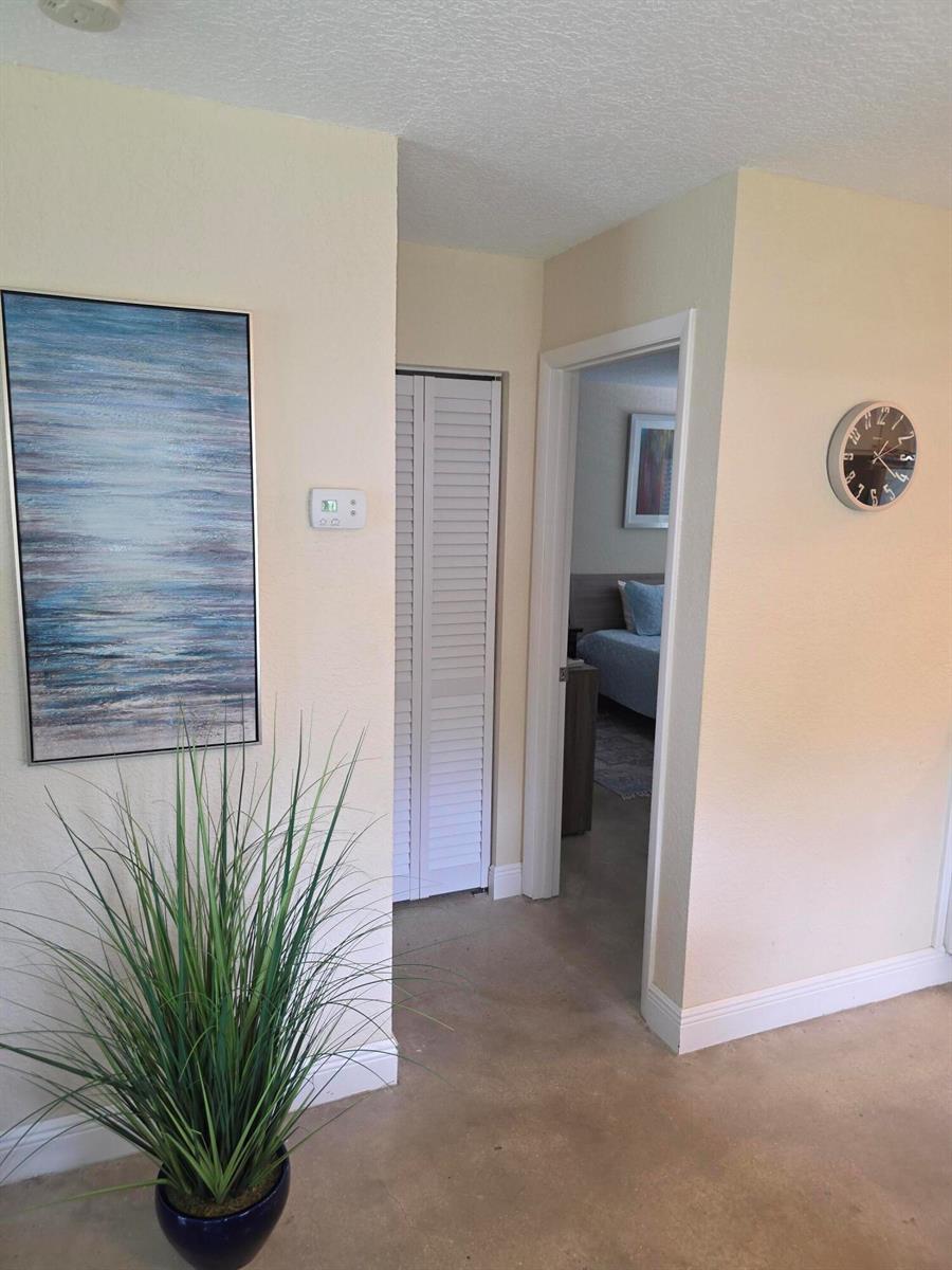 A hallway with a potted plant, wall art, a thermostat, and a doorway to a bedroom — 207 Tropic Isle Drive # 215, Delray Beach FL 33483, DELRAY BEACH, FL