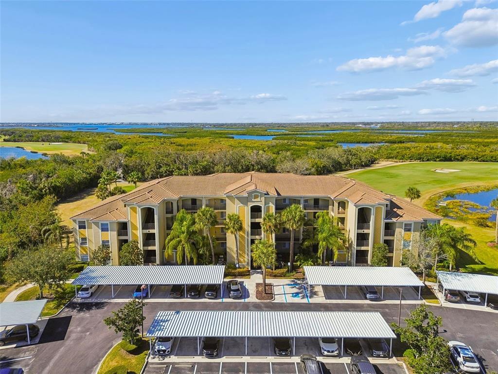 An aerial view of a multi-story apartment building surrounded by a golf course and water — 7607 GRAND ESTUARY TRAIL UNIT 302, BRADENTON, FL