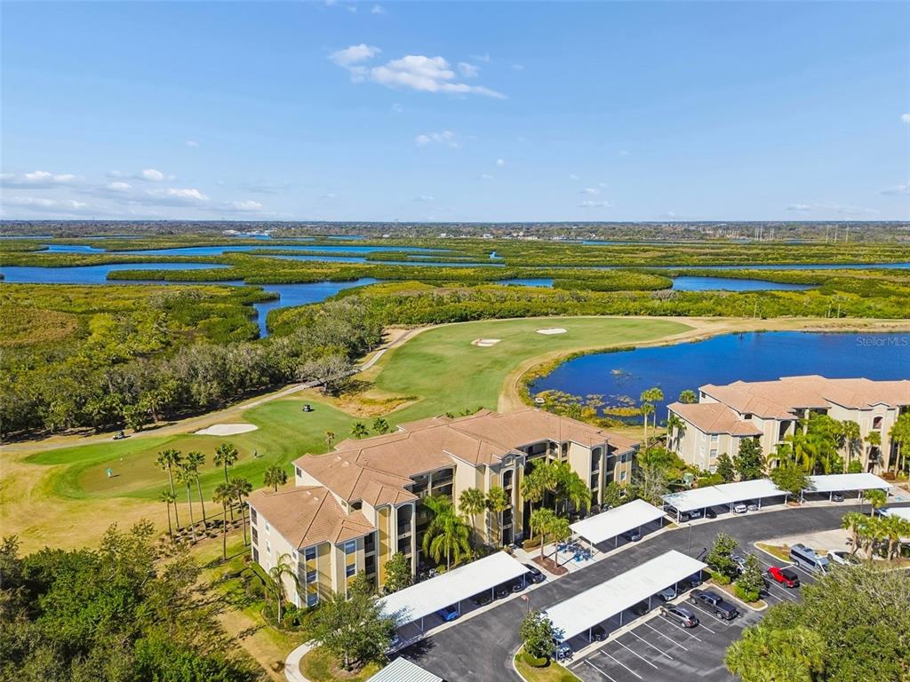 An aerial view shows a multi-story apartment building next to a golf course and lake — 7607 GRAND ESTUARY TRAIL UNIT 302, BRADENTON, FL