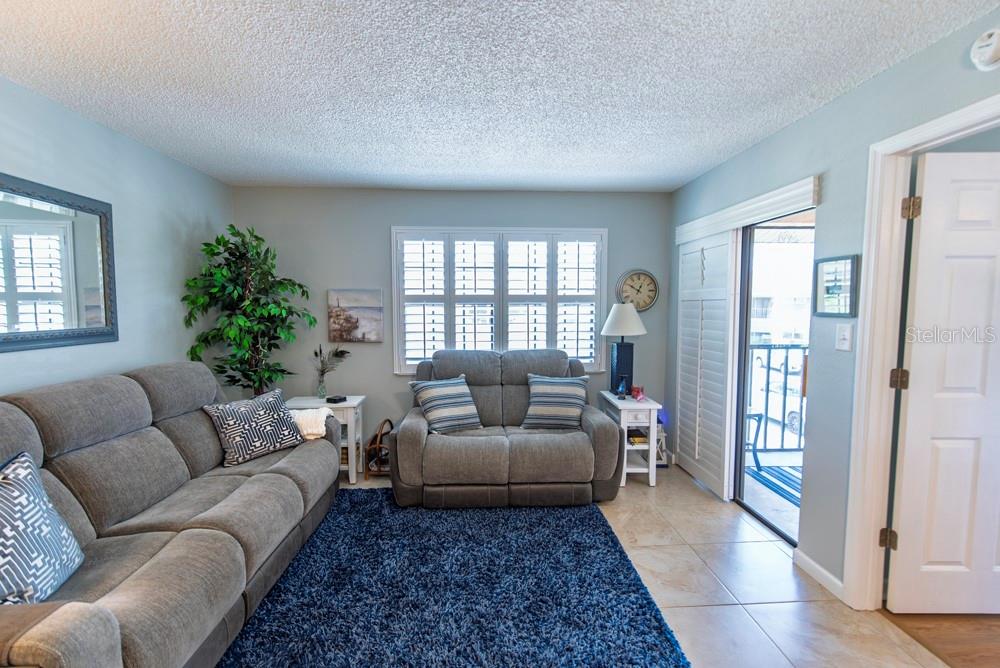 A living room features gray sofas, a blue area rug, and a sliding glass door — 19505 QUESADA AVENUE UNIT RR202, PORT CHARLOTTE, FL