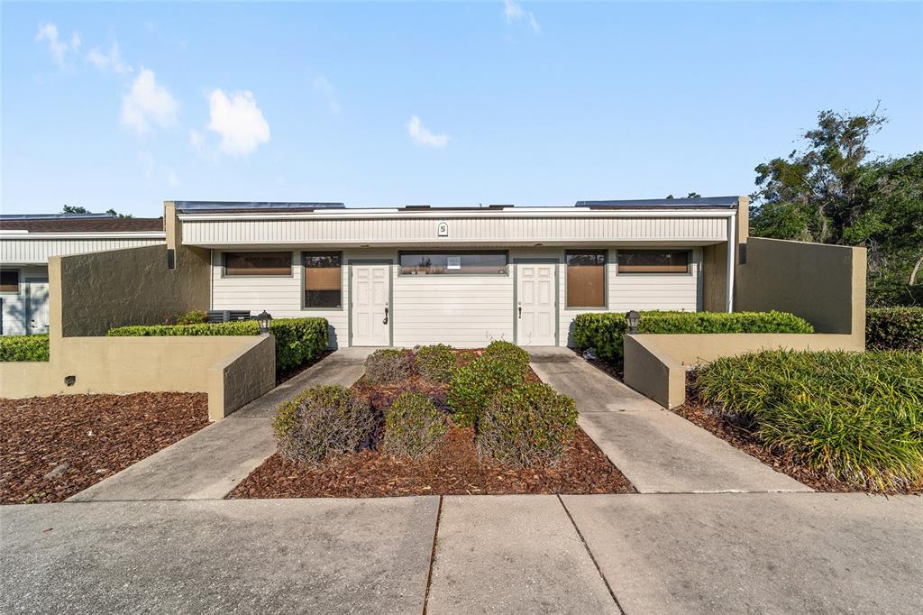 A single-story duplex building features two white doors, horizontal siding, and a landscaped front yard — 2801 SW COLLEGE ROAD UNIT 5, OCALA, FL