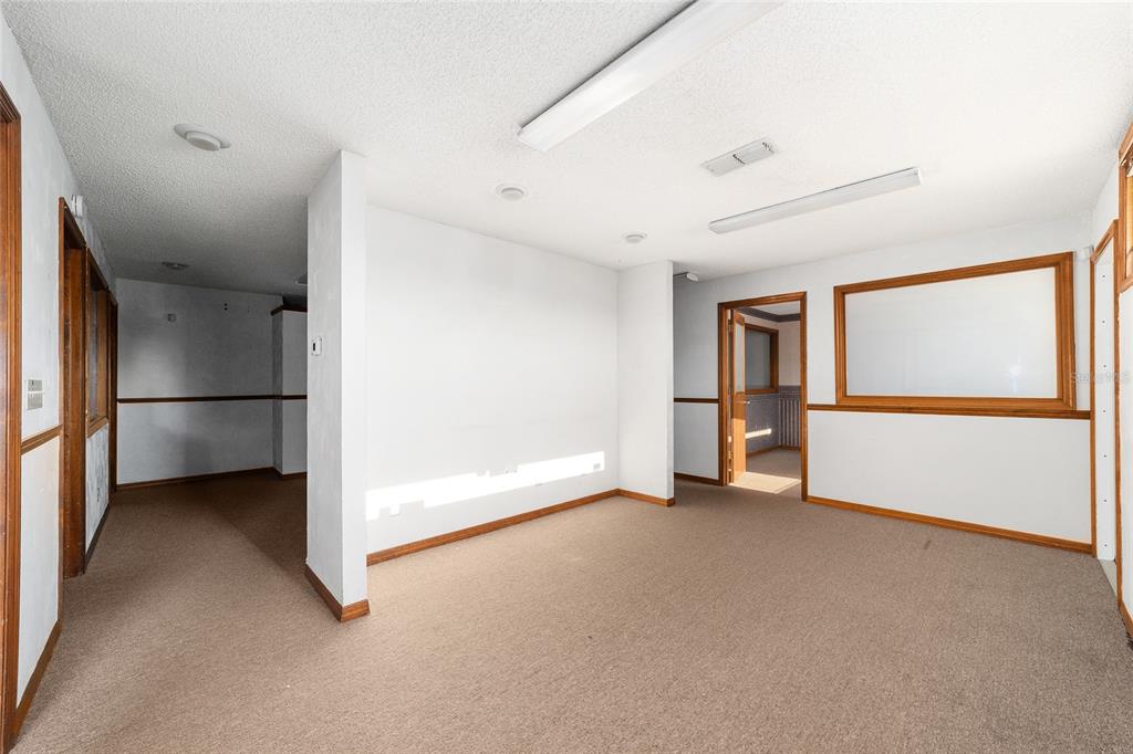 An empty room with beige carpet, white walls, wood trim, and fluorescent ceiling lights — 2801 SW COLLEGE ROAD UNIT 5, OCALA, FL
