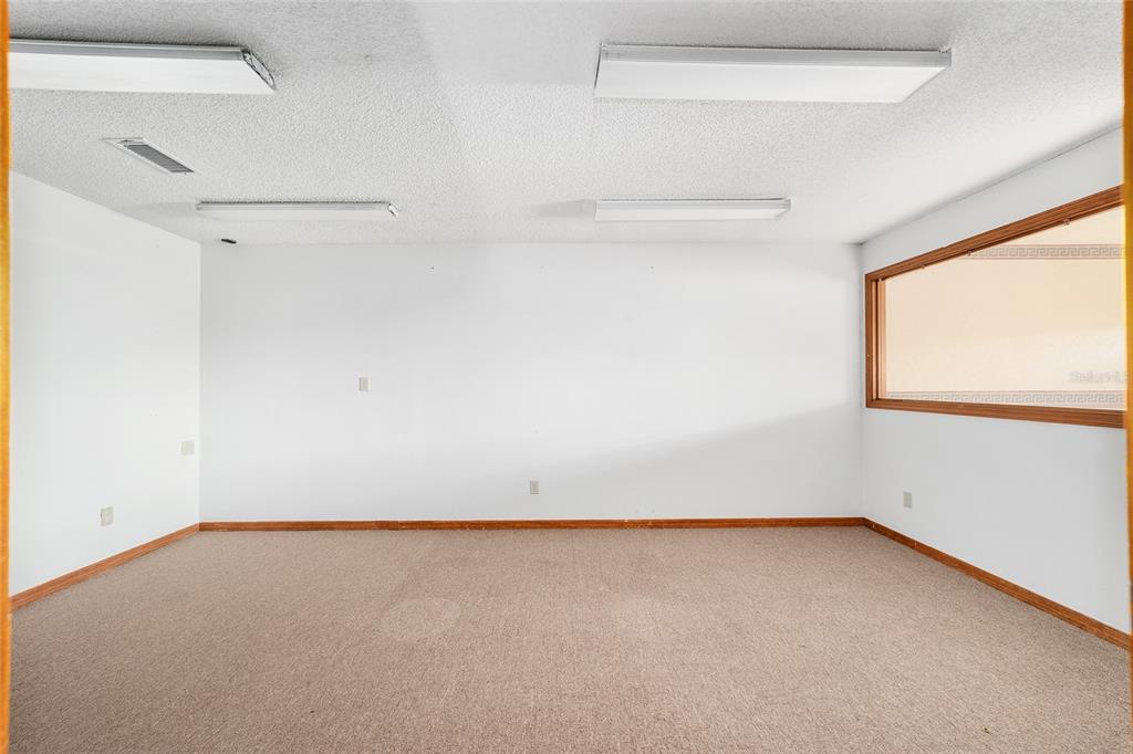 An empty room with beige carpet, white walls, wood trim, and four ceiling light fixtures — 2801 SW COLLEGE ROAD UNIT 5, OCALA, FL