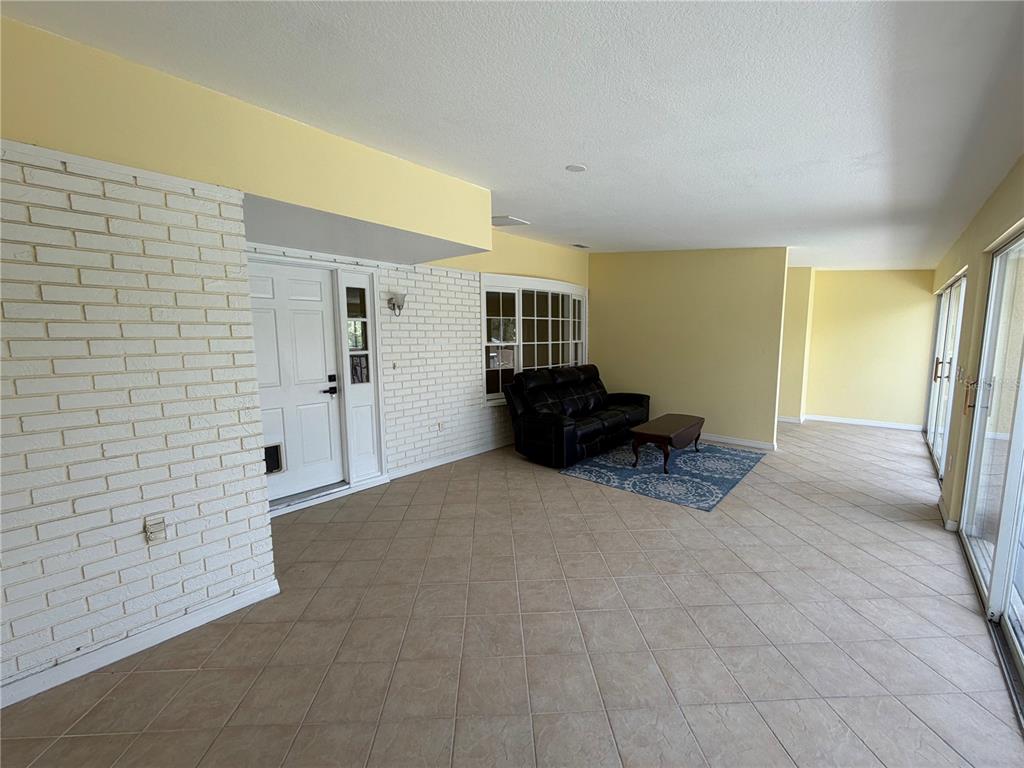 A sunroom features light-colored tile flooring, yellow walls, a white brick accent wall, and a sofa — 7941 SYCAMORE DRIVE, NEW PORT RICHEY, FL