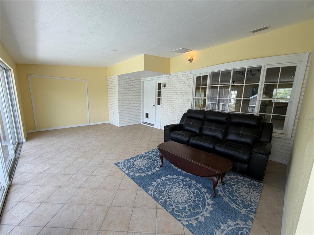 A sunroom features tile flooring, a white brick wall, and a black leather sofa — 7941 SYCAMORE DRIVE, NEW PORT RICHEY, FL