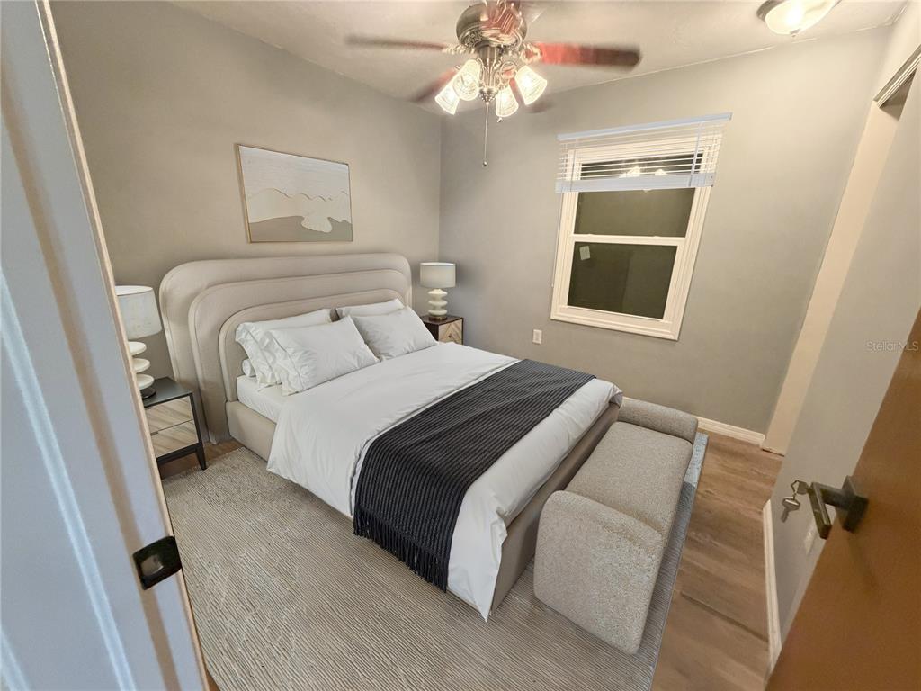 A bedroom features a queen bed with a gray upholstered headboard and a ceiling fan — 7941 SYCAMORE DRIVE, NEW PORT RICHEY, FL