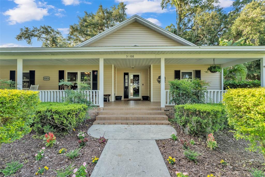 A tan house with a wide front porch, white railings, and a concrete walkway — 5108 WATERWOOD DRIVE, BARTOW, FL