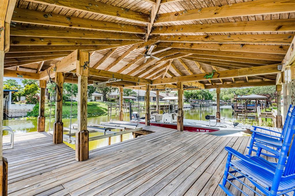 A covered wooden boat dock features a boat slip, a ceiling fan, and blue rocking chairs — 1811 MISSOURI AVENUE, SANFORD, FL