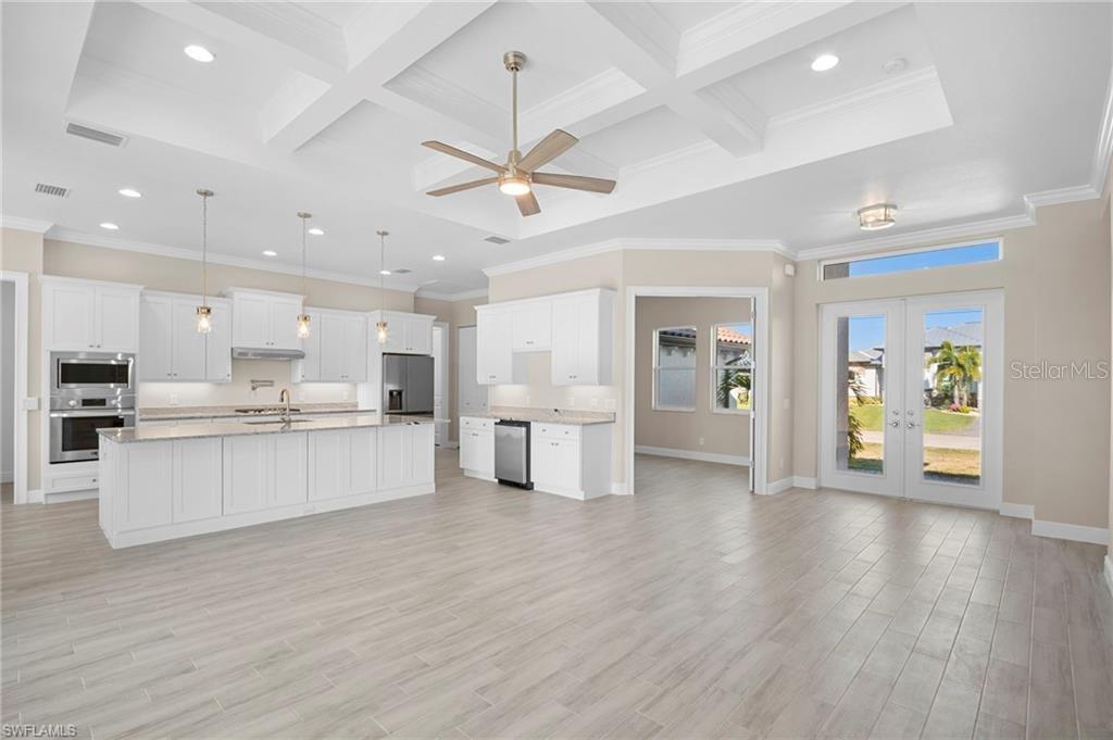 A bright, open-concept kitchen features white cabinetry, a large island, and light wood-look flooring — 15698 MEACHAM CIRCLE, PORT CHARLOTTE, FL