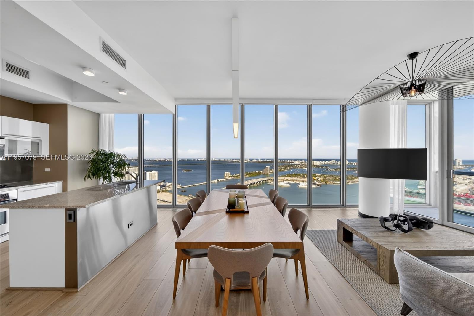 A modern dining area features a wooden table, floor-to-ceiling windows, and a panoramic water view — 888 Biscayne Blvd # 5508, Miami FL 33132, MIAMI, FL