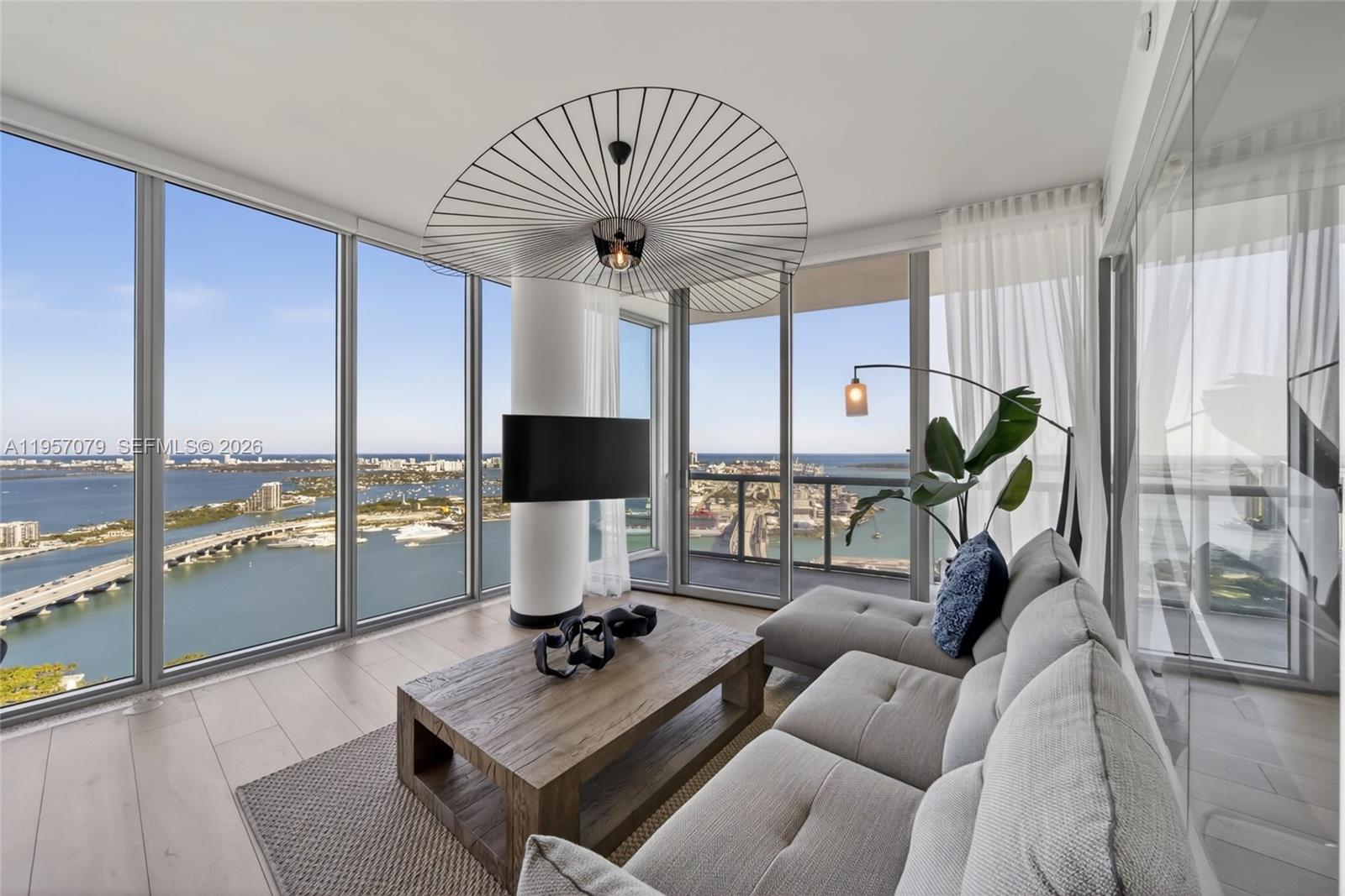 A modern living room features floor-to-ceiling windows, a sectional sofa, and panoramic bay views — 888 Biscayne Blvd # 5508, Miami FL 33132, MIAMI, FL