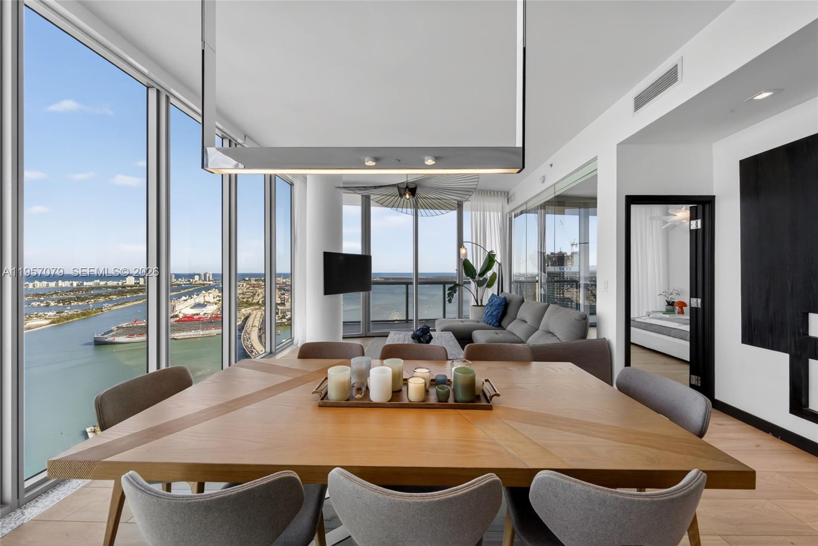 A dining area with a wooden table and chairs overlooks a coastal city and harbor — 888 Biscayne Blvd # 5508, Miami FL 33132, MIAMI, FL