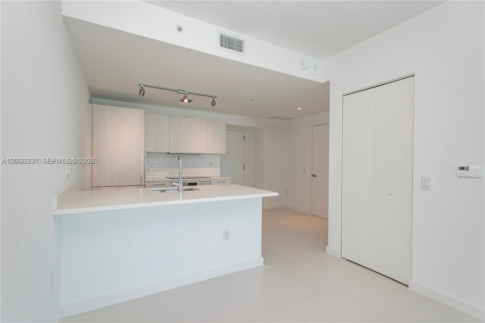 A modern kitchen features white cabinetry, a quartz countertop island, and light-colored tile flooring — 501 NE 31st St # 3505, Miami FL 33137, MIAMI, FL