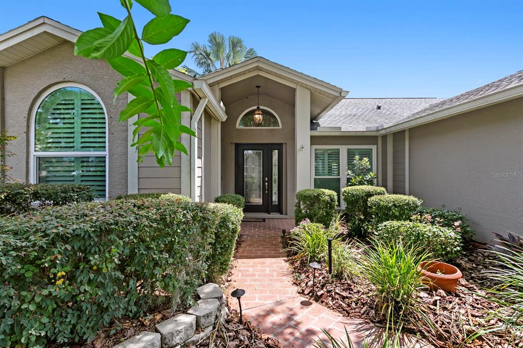 A brick walkway leads to the front entrance of a house with beige stucco siding — 14607 VILLAGE GLEN CIRCLE, TAMPA, FL