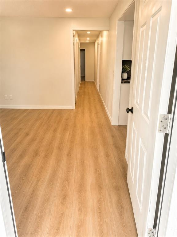 A hallway with light wood-look flooring leads to a doorway at the end — 1016 W 8TH STREET, SANFORD, FL