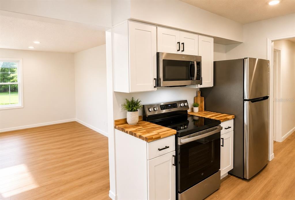 A kitchen features white cabinets, butcher block countertops, stainless steel appliances, and light wood flooring — 1016 W 8TH STREET, SANFORD, FL