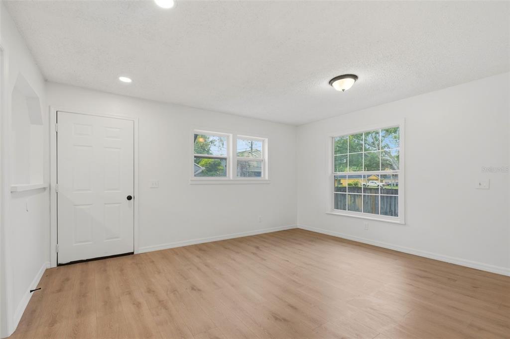 An empty room with white walls, light wood-look flooring, two windows, and a white door — 1016 W 8TH STREET, SANFORD, FL