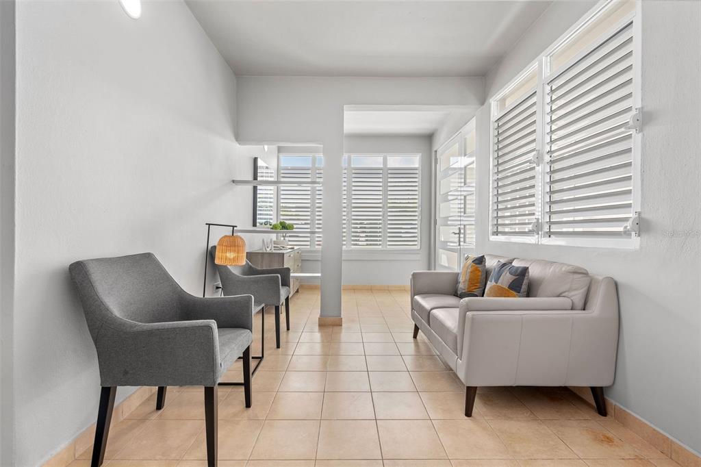 A sunroom with tile flooring, a light gray sofa, two gray armchairs, and plantation shutters — 56 MARIA MOCZO UNIT 1, SAN JUAN, PR