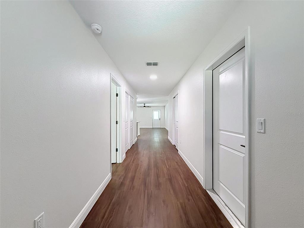A long hallway with wood-look flooring leads toward a bright room with a white door — 5987 W OAK PARK BOULEVARD, HOMOSASSA, FL