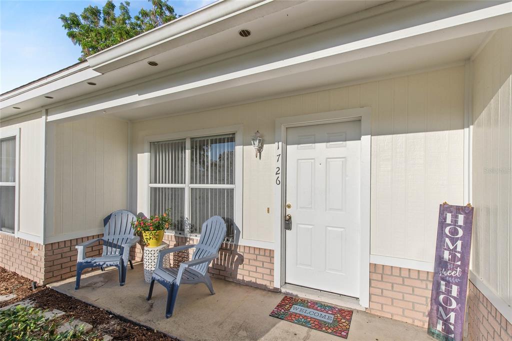 A front porch with two blue Adirondack chairs, a potted plant, and a white door — 1726 TROPICAL COURT, TAVARES, FL