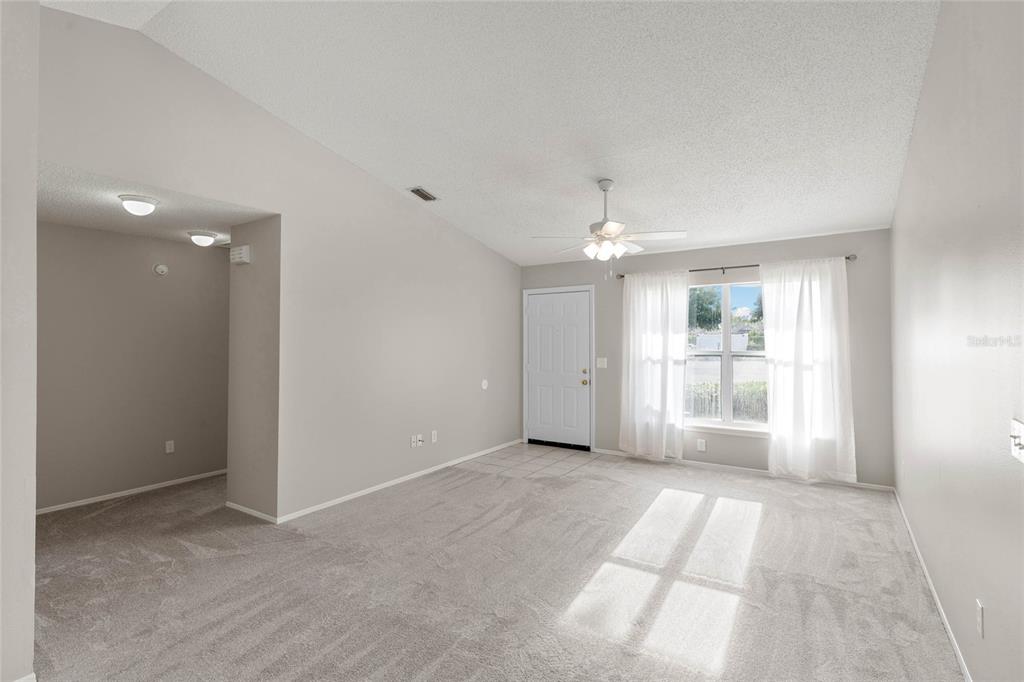 A living room with gray carpet, light walls, a ceiling fan, and a front door — 1726 TROPICAL COURT, TAVARES, FL