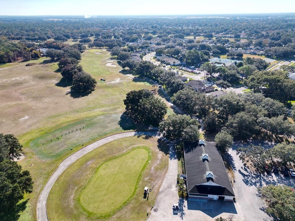 An aerial view shows a golf course green, a clubhouse building, and surrounding residential neighborhoods — 4460 GOLF CLUB LANE, SPRING HILL, FL