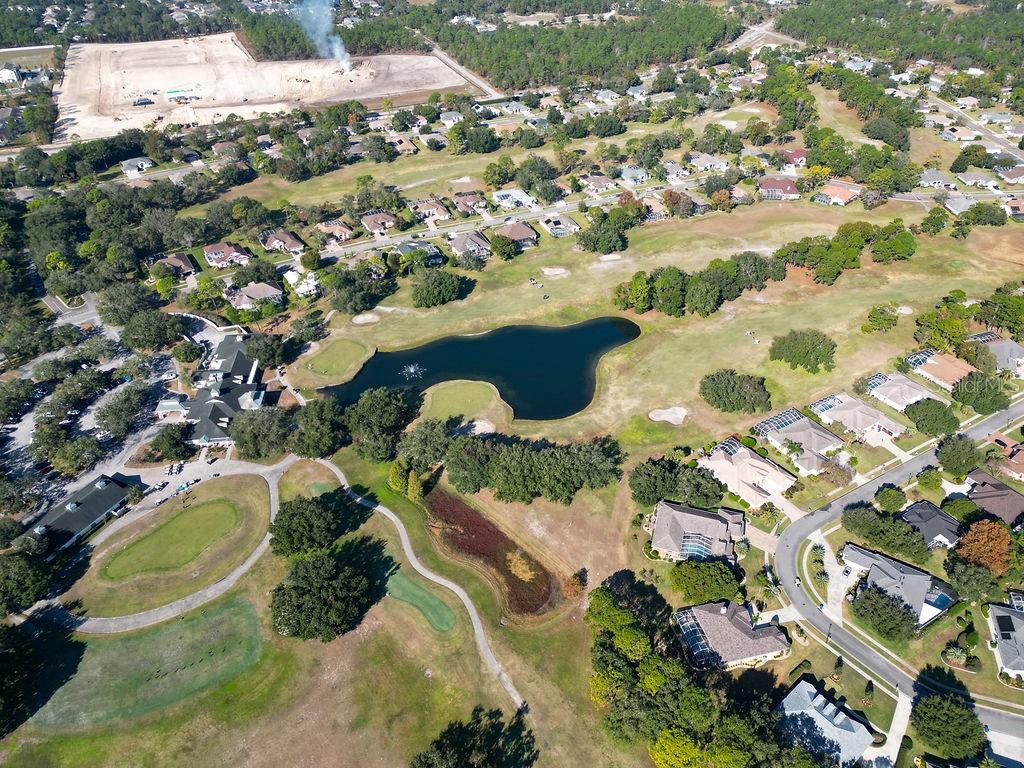 Aerial view of a golf course with a central pond surrounded by residential homes — 4460 GOLF CLUB LANE, SPRING HILL, FL