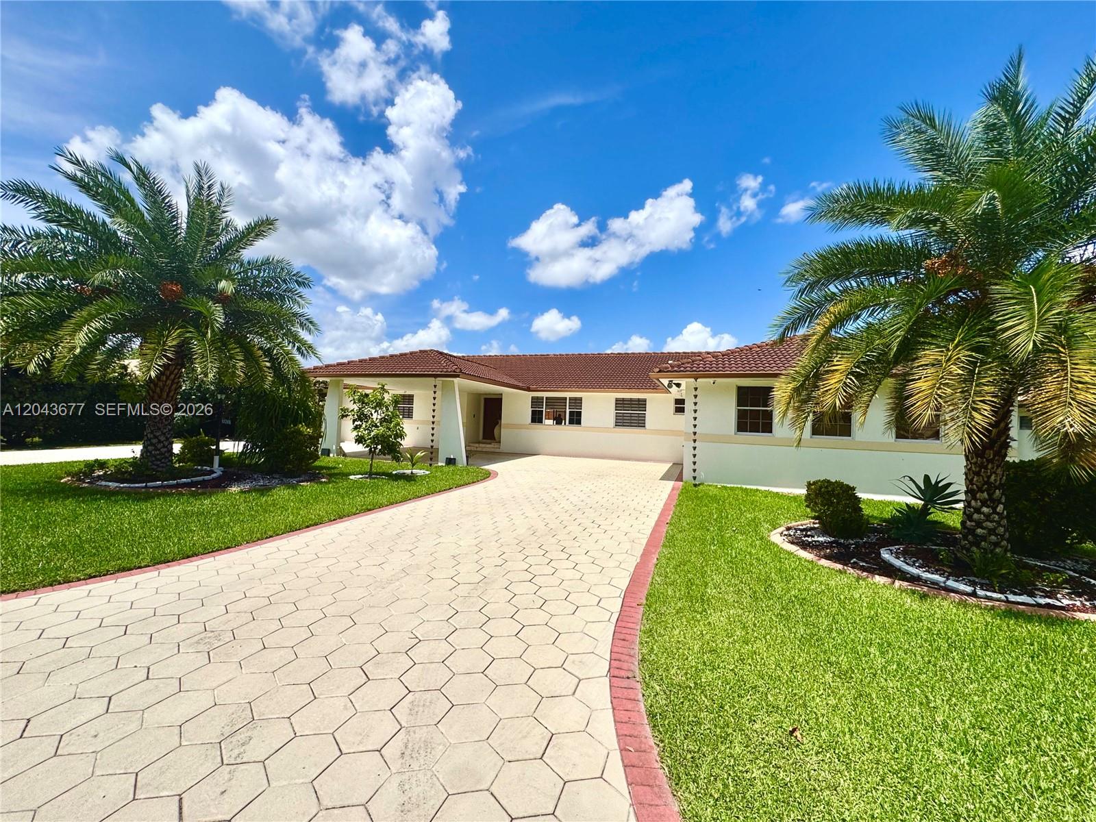 A single-story house with a tiled roof and a paved driveway sits between two palm trees — 18701 Wentworth Dr, Hialeah FL 33015, HIALEAH, FL