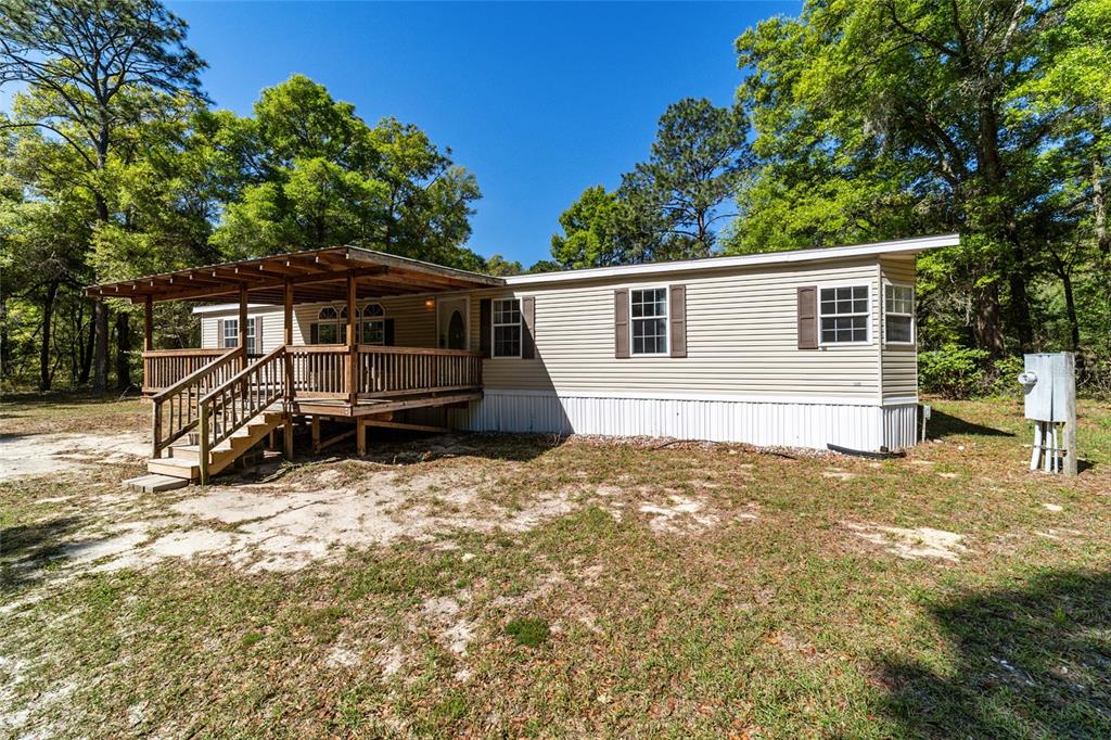 A beige mobile home features a wooden deck with a covered porch and surrounding trees — 8415 SW 41ST PLACE ROAD, OCALA, FL