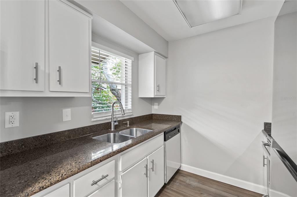 A kitchen features white cabinets, dark granite countertops, a stainless steel sink, and wood-look flooring — 308 DORCHESTER SQUARE, LAKE MARY, FL