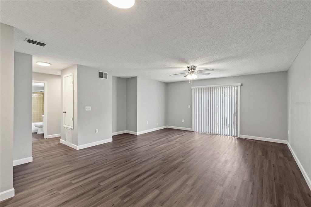 An empty living room with gray walls, dark wood-look flooring, and a sliding glass door — 308 DORCHESTER SQUARE, LAKE MARY, FL