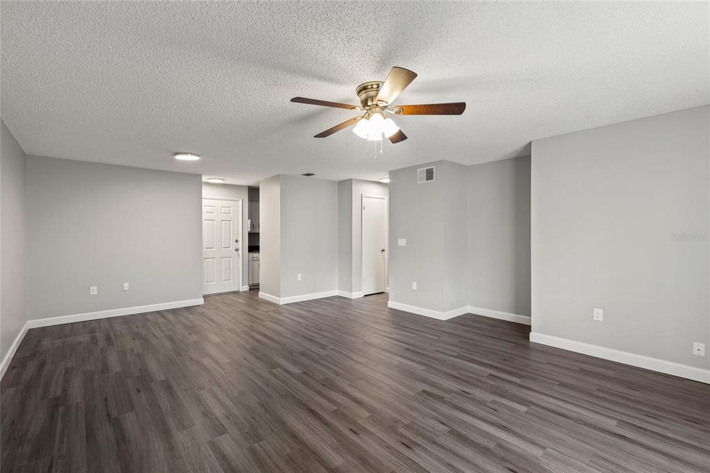 A spacious, empty living room features gray walls, wood-look flooring, and a ceiling fan — 308 DORCHESTER SQUARE, LAKE MARY, FL