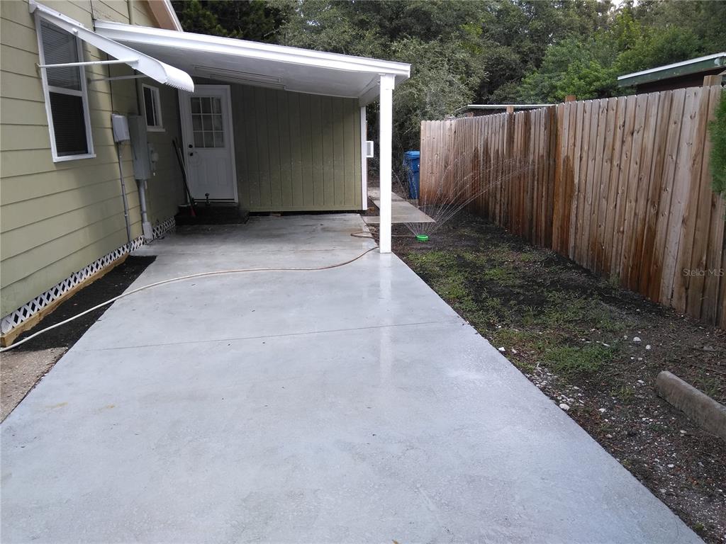 A concrete patio sits under a covered carport next to a house and wooden fence — 910 9TH AVENUE SW, LARGO, FL