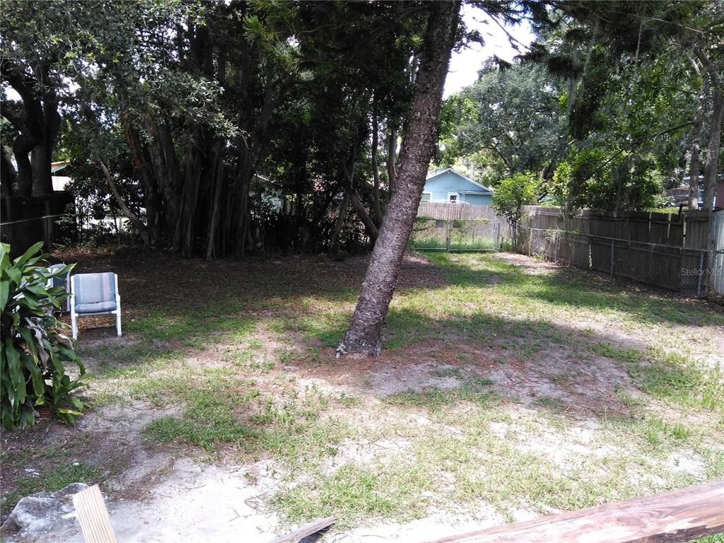 A backyard features a large tree, patchy grass, a wooden fence, and a patio chair — 910 9TH AVENUE SW, LARGO, FL