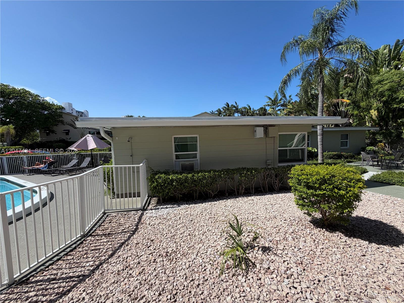 The exterior of a single-story building features light-colored siding, windows, and a gravel landscape — 3230 NE 13th St # 2, Pompano Beach FL 33062, POMPANO BEACH, FL