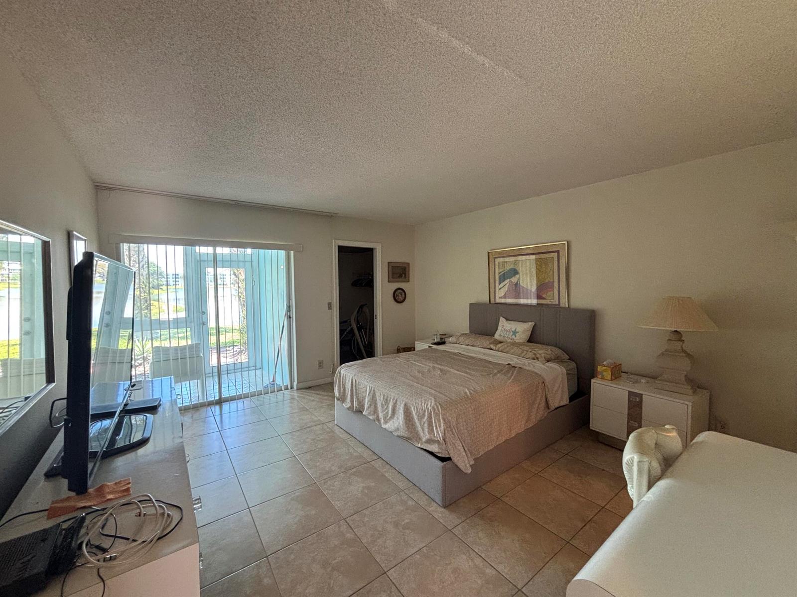 A bedroom features a gray upholstered bed, tile flooring, and a sliding glass door — 105 E Wellington # 105, West Palm Beach FL 33417, WEST PALM BEACH, FL