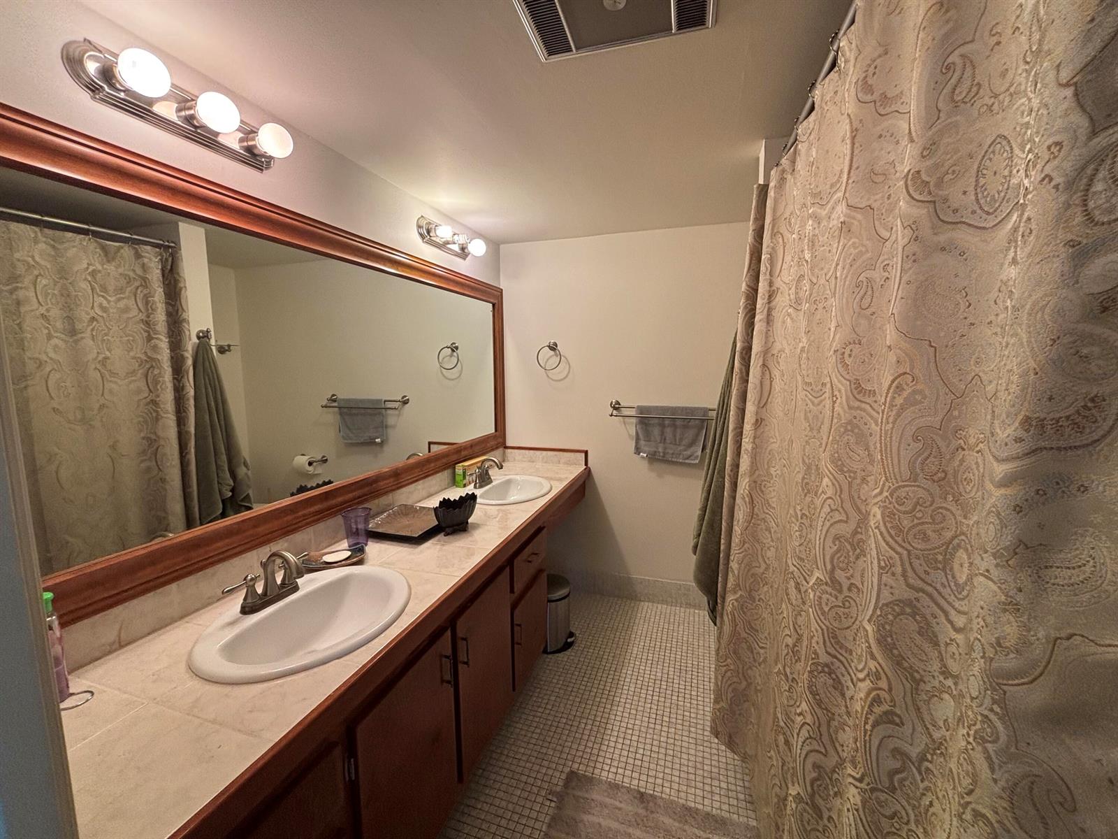 A bathroom features a double vanity with wood cabinets, tiled countertops, and a large mirror — 105 E Wellington # 105, West Palm Beach FL 33417, WEST PALM BEACH, FL