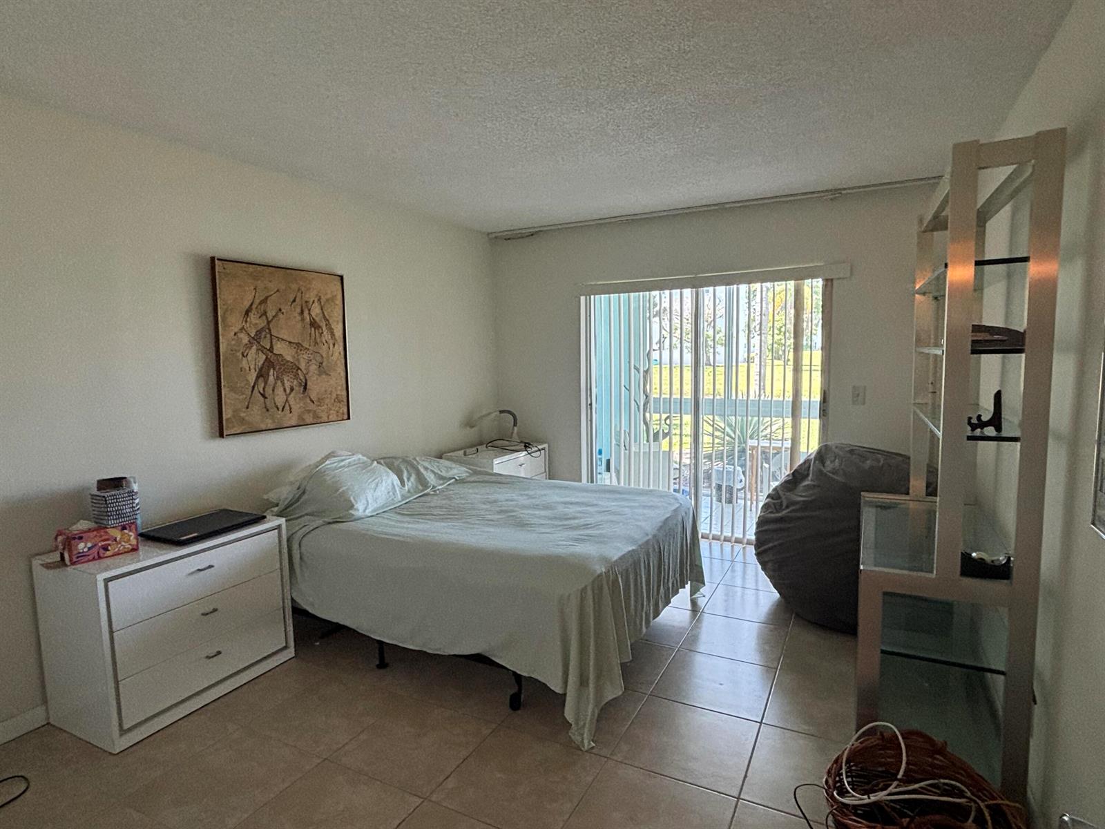 A bedroom with tile floors, a bed, a dresser, a beanbag chair, and sliding glass doors — 105 E Wellington # 105, West Palm Beach FL 33417, WEST PALM BEACH, FL