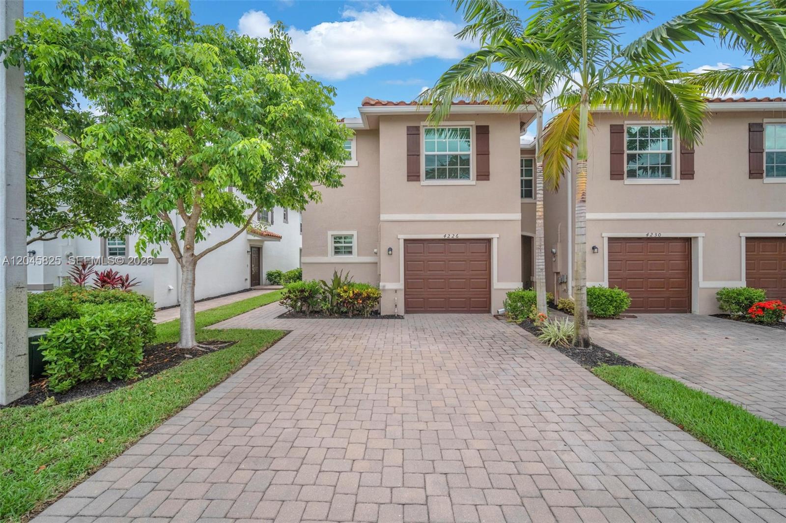 A two-story townhouse with a paved driveway, brown garage door, and palm tree in front — 4226 Bent River Rd, Lake Worth FL 33467, LAKE WORTH, FL