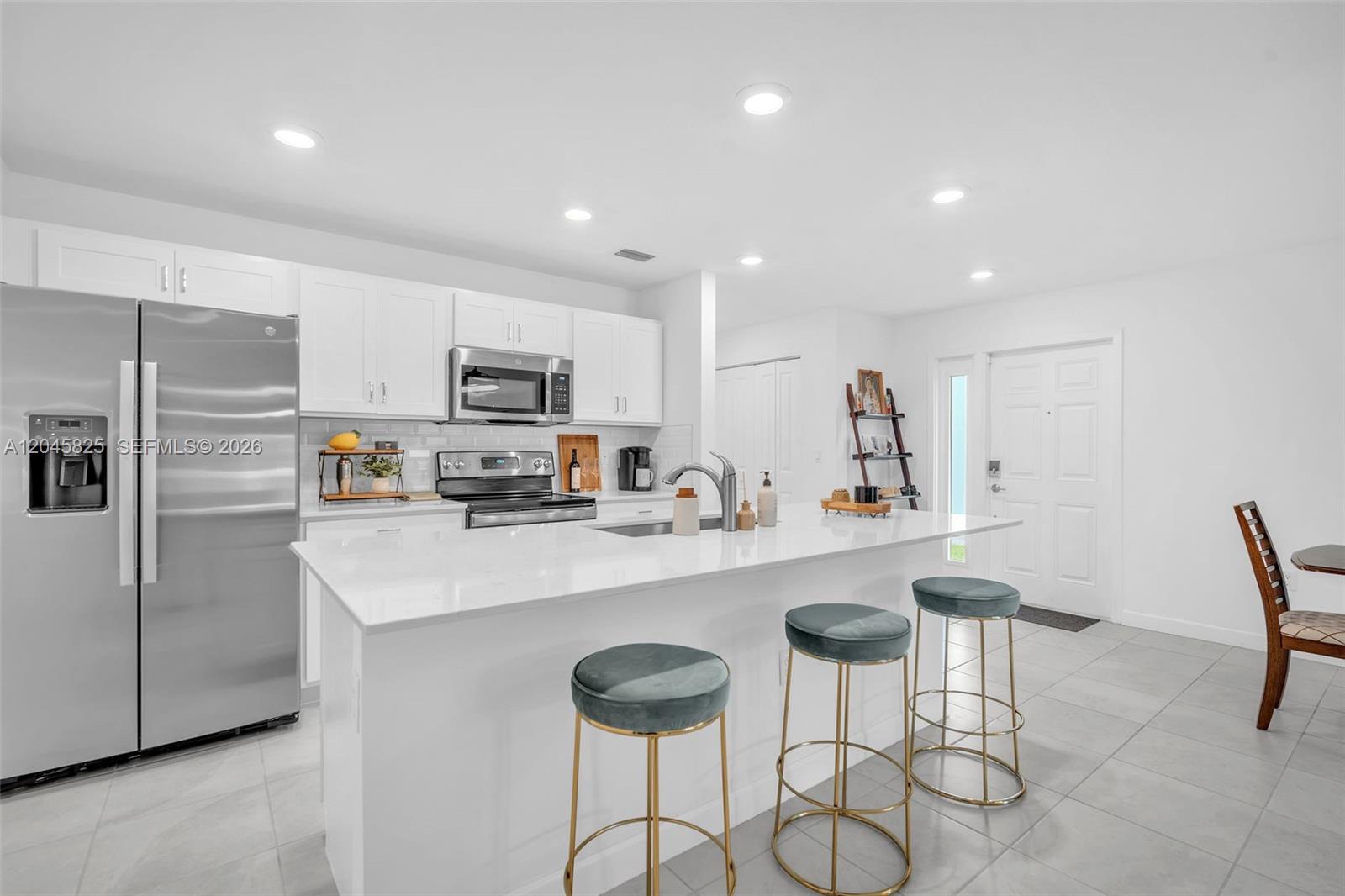 A modern kitchen features white cabinets, stainless steel appliances, and a large quartz island — 4226 Bent River Rd, Lake Worth FL 33467, LAKE WORTH, FL