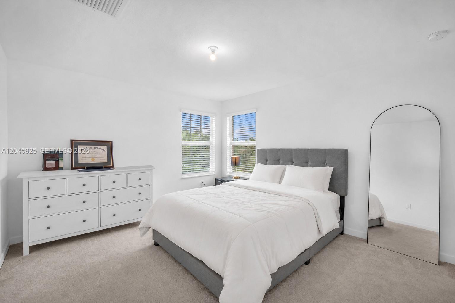 A bedroom features a gray upholstered bed, a white dresser, and a large arched floor mirror — 4226 Bent River Rd, Lake Worth FL 33467, LAKE WORTH, FL
