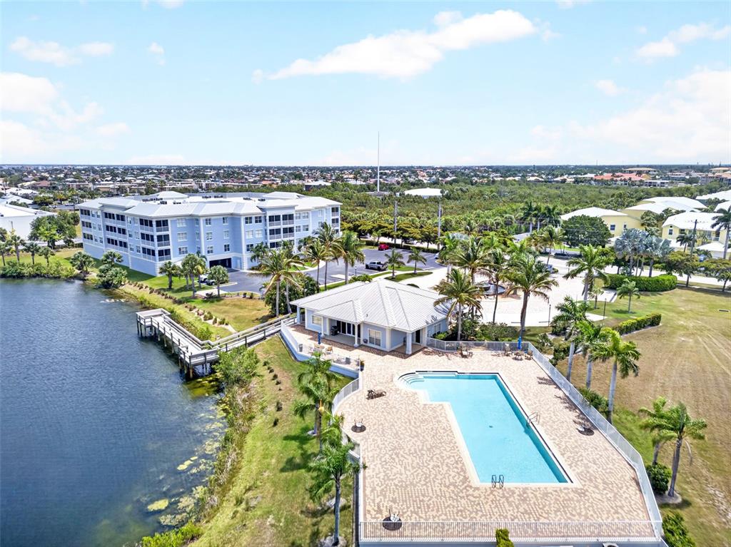 An aerial view shows a swimming pool, clubhouse, and multi-story apartment building near a lake — 2001 BAL HARBOR BOULEVARD UNIT 2308, PUNTA GORDA, FL