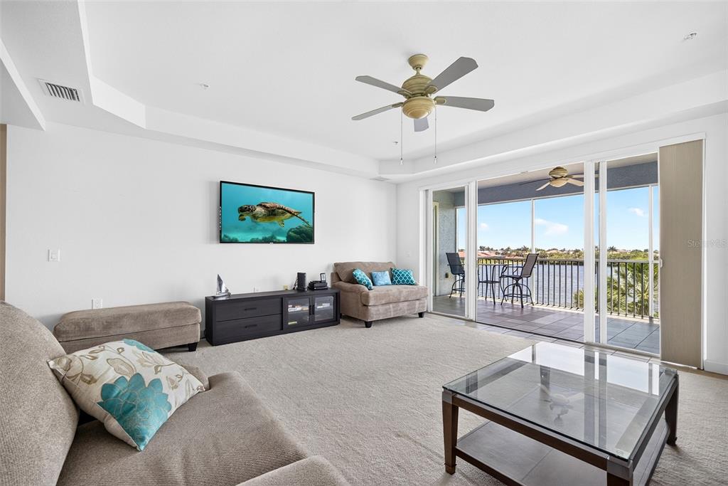 A living room features beige carpet, a television, a glass coffee table, and a balcony — 2001 BAL HARBOR BOULEVARD UNIT 2308, PUNTA GORDA, FL