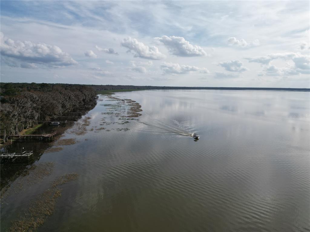 An aerial view shows a boat traveling on a large lake beside a wooded shoreline — 13813 SE 201ST TERRACE, HAWTHORNE, FL