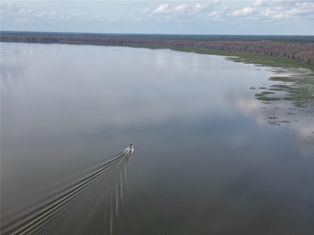 An aerial view of a boat traveling across a large lake near a wooded shoreline — 13813 SE 201ST TERRACE, HAWTHORNE, FL